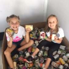 two girls sitting around a pile of cans