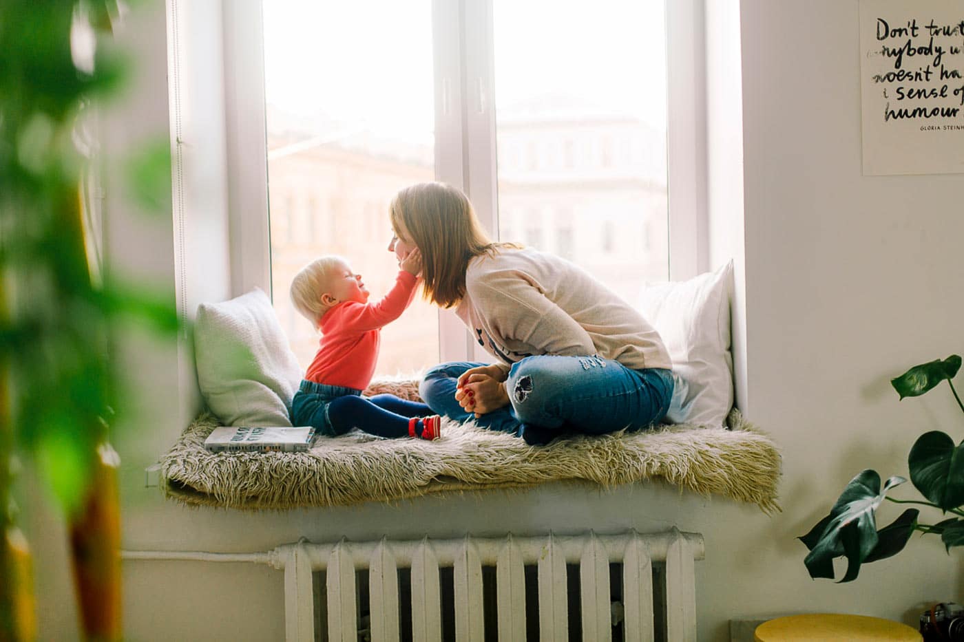 a mom with her toddler looking at her in front of a window touching the moms face