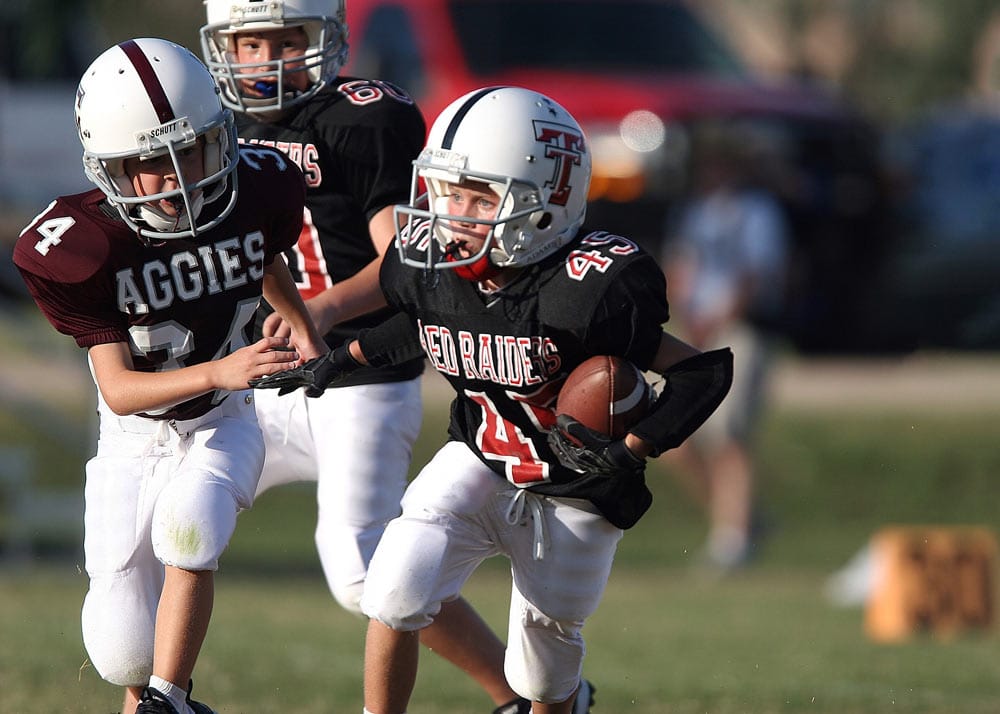 a photo of a young football player wearing a mouth guard running with the ball