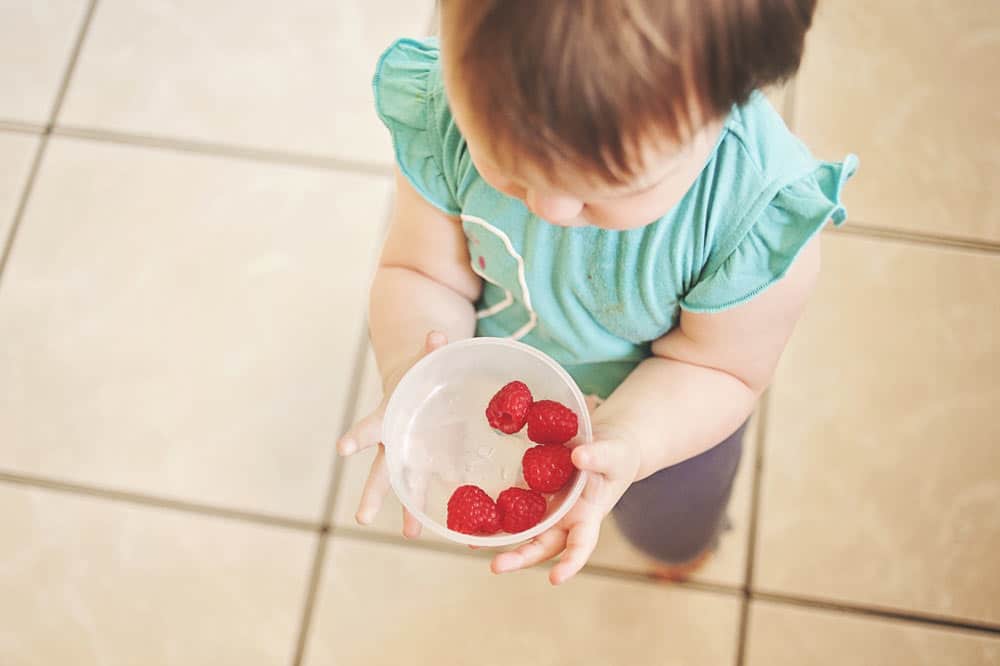A toddler holding a container with raspberries
