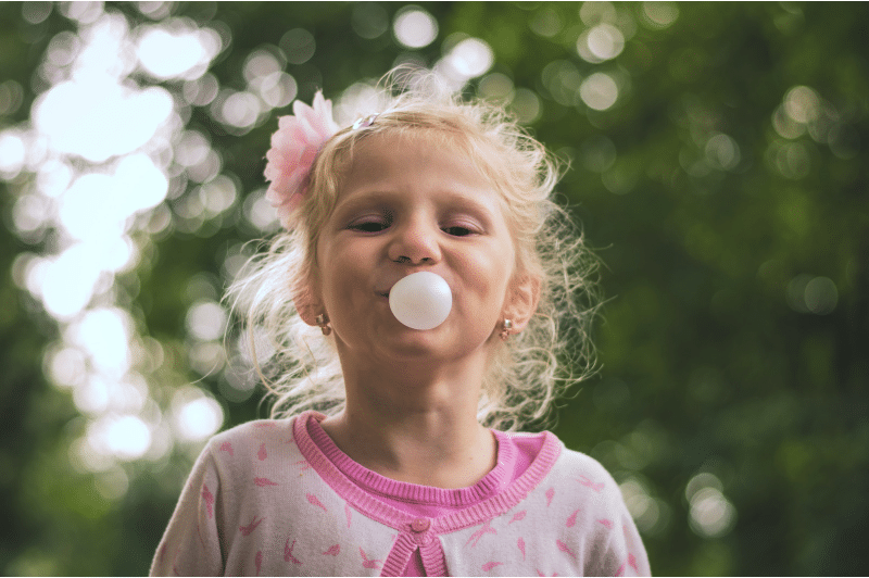A young girl blowing a bubble with bubble gum