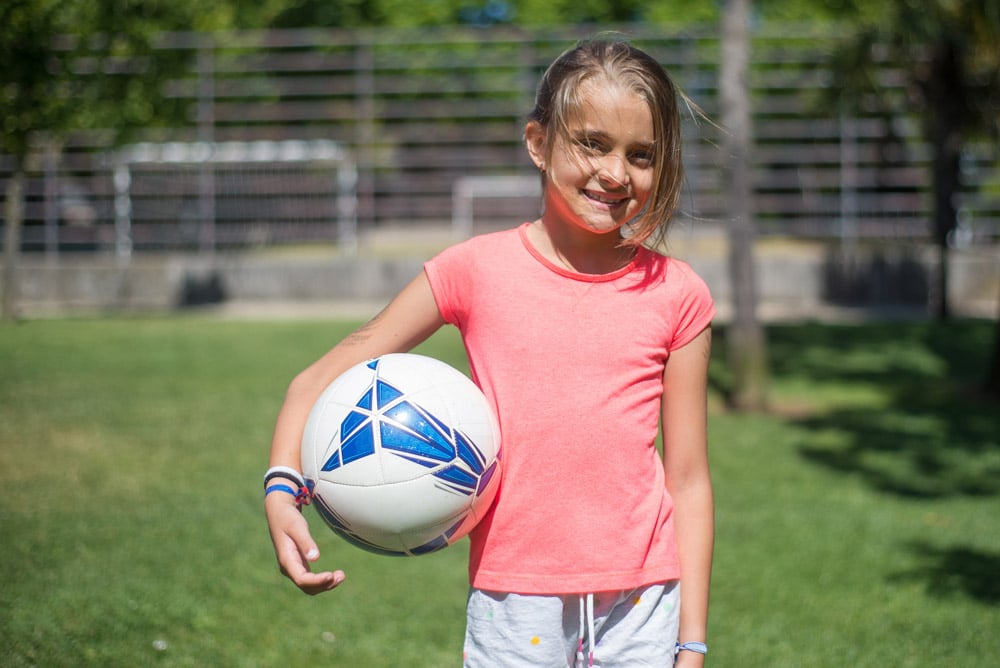 A young girl holding a soccer ball on a grass field